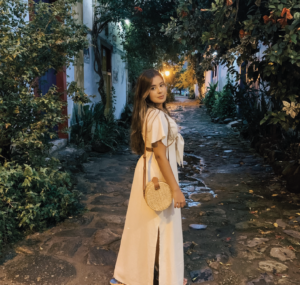 Mulher com vestido branco em uma rua de pedras rodeada por flores